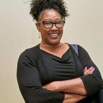 Smiling woman in black top with arms crossed against a plain background