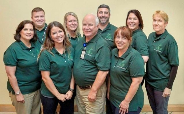 Nine people in green polo shirts posing together in an office hallway.