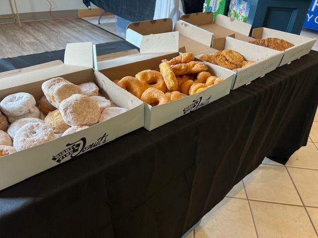 Table of assorted donuts in open boxes on a black tablecloth at a bakery display
