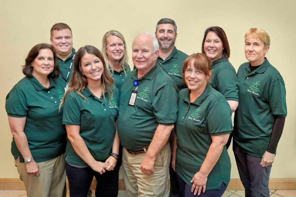 Group of staff in green shirts posing together indoors against a plain wall