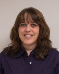 Smiling woman with shoulder-length brown hair in a dark purple shirt against a plain background