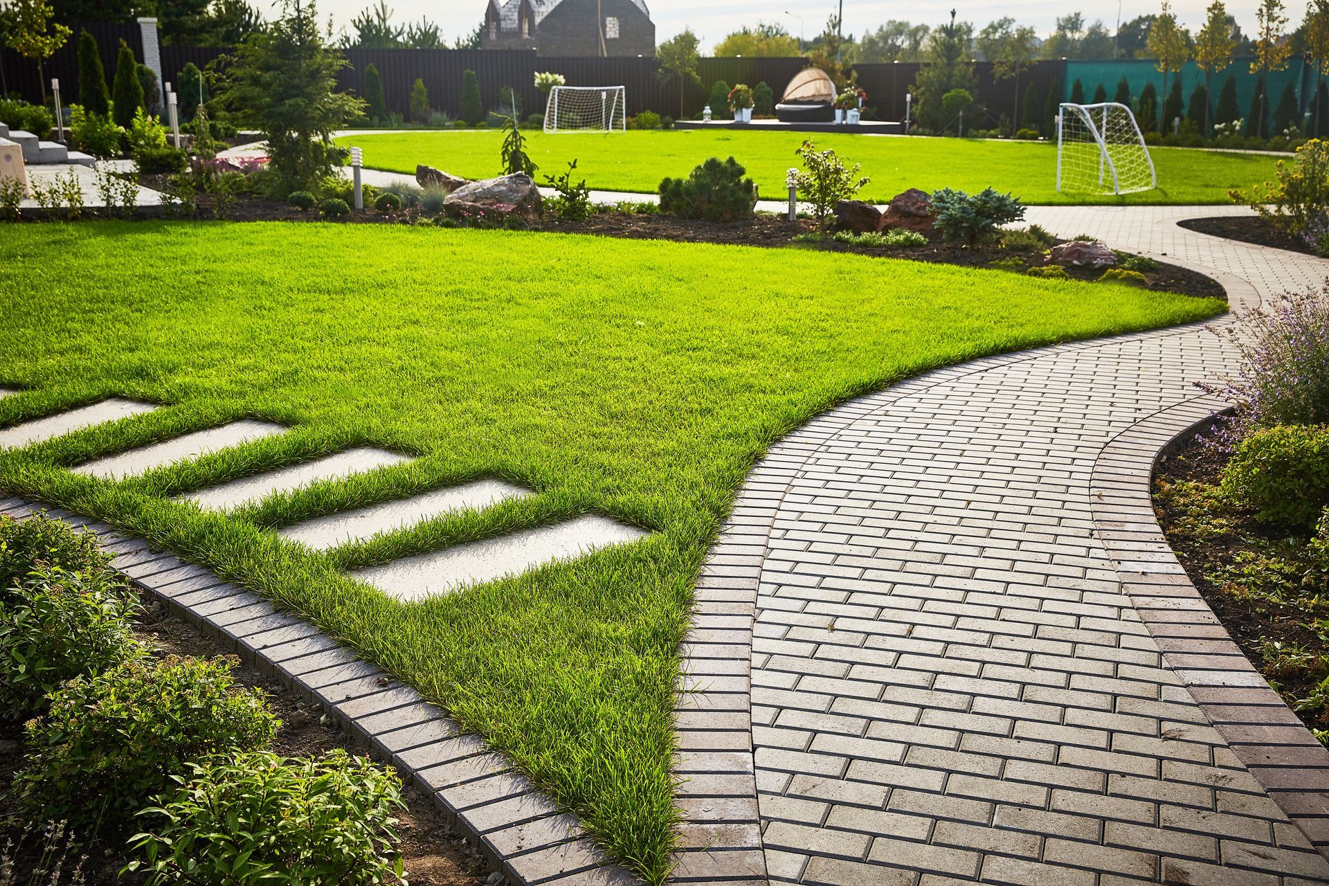 A brick walkway leading to a lush green field in a garden.