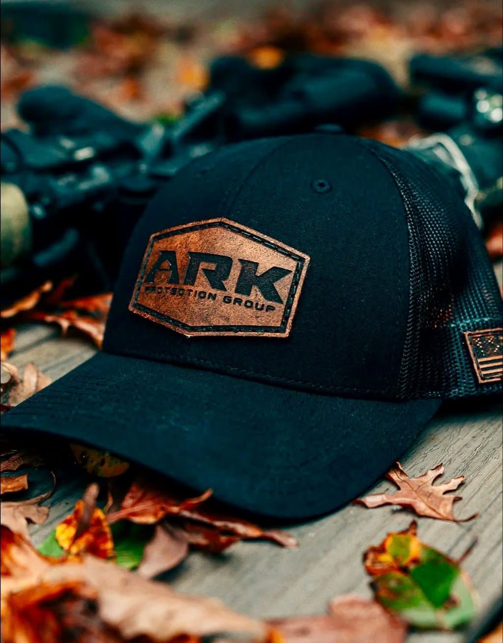 Black ARK baseball cap on a rustic wooden surface with autumn leaves