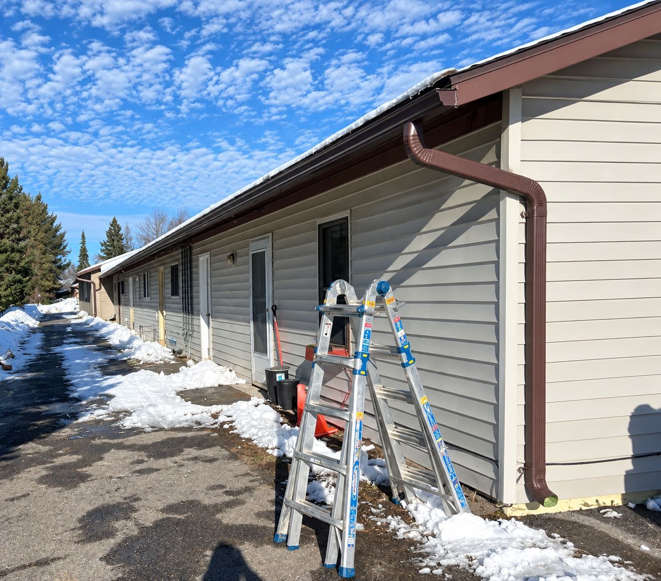 Snowy apartment building exterior with ladders and a worker near the wall