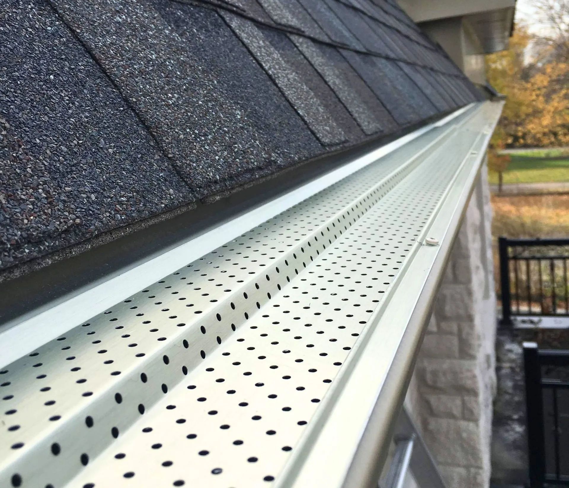 White perforated roof gutter beneath dark shingle roof on a house side exterior