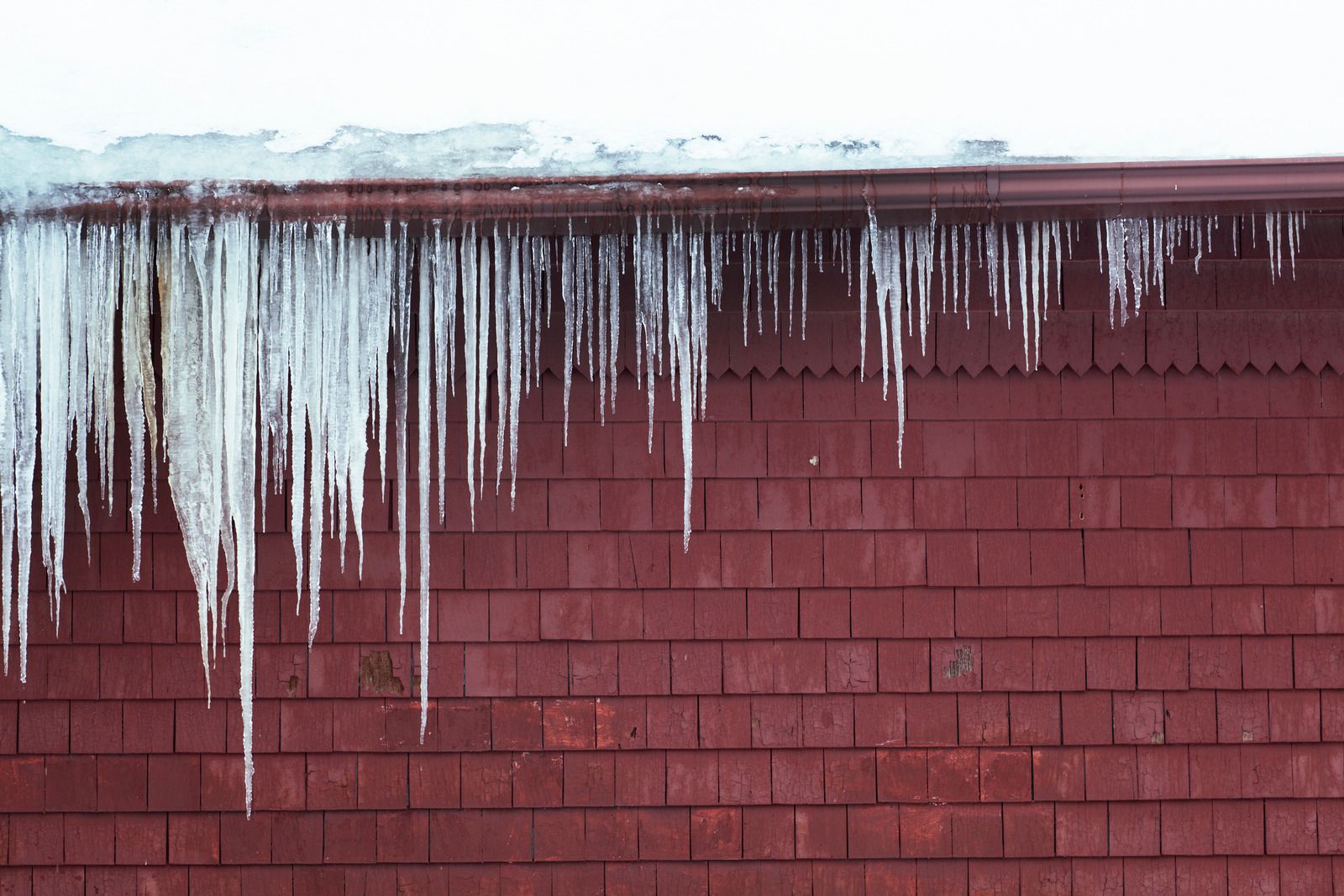 Icicles hanging from a red brick wall under a snowy roof edge