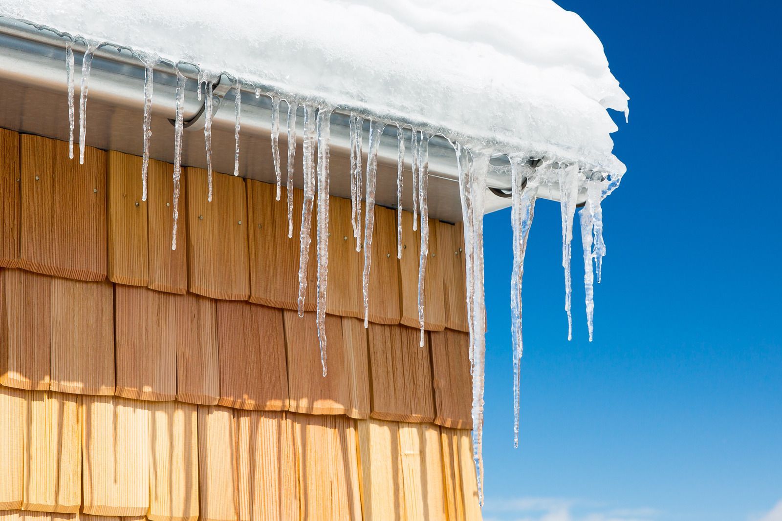 Snow-covered roof with long icicles against a bright blue sky