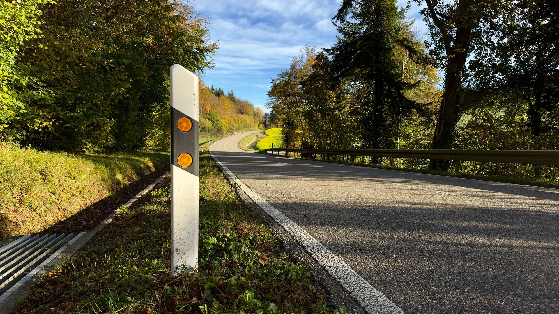 Winding country road curving through autumn trees with a roadside mile marker post in the foreground