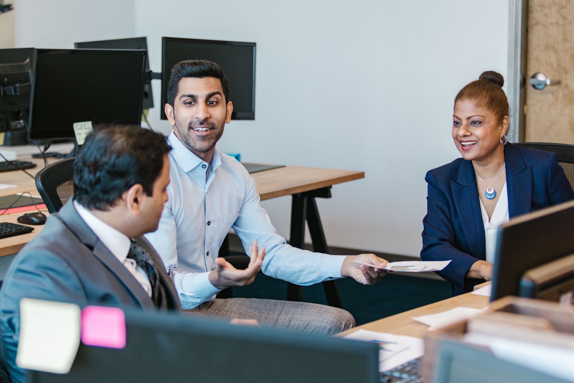 Two businessmen with a businesswoman talking at a desk with computers