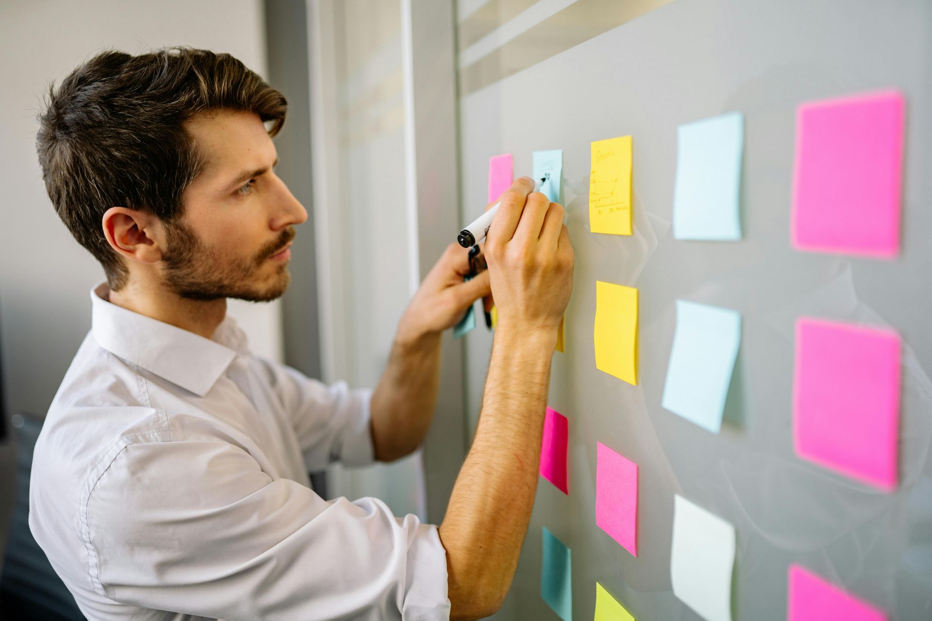 Man at wall with marker writing on post-it notes
