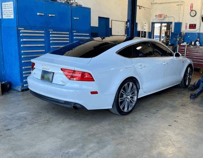 White Audi coupe in an auto repair shop next to blue tool cabinets
