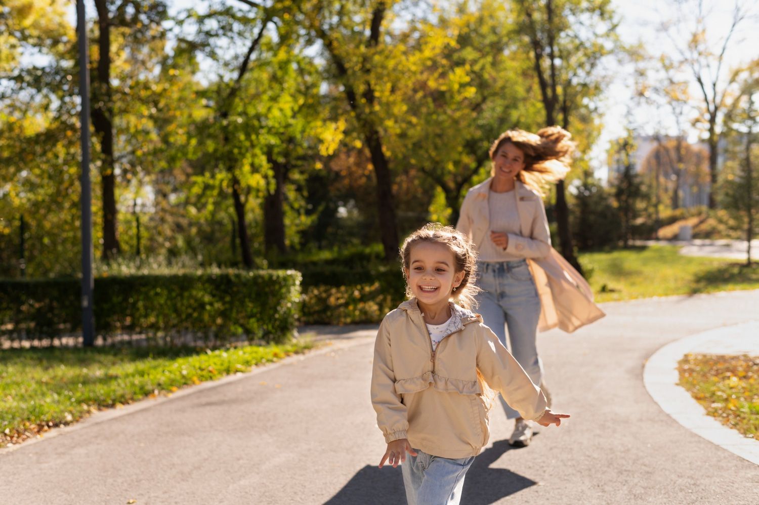 A woman and a little girl are running down a road in a park.