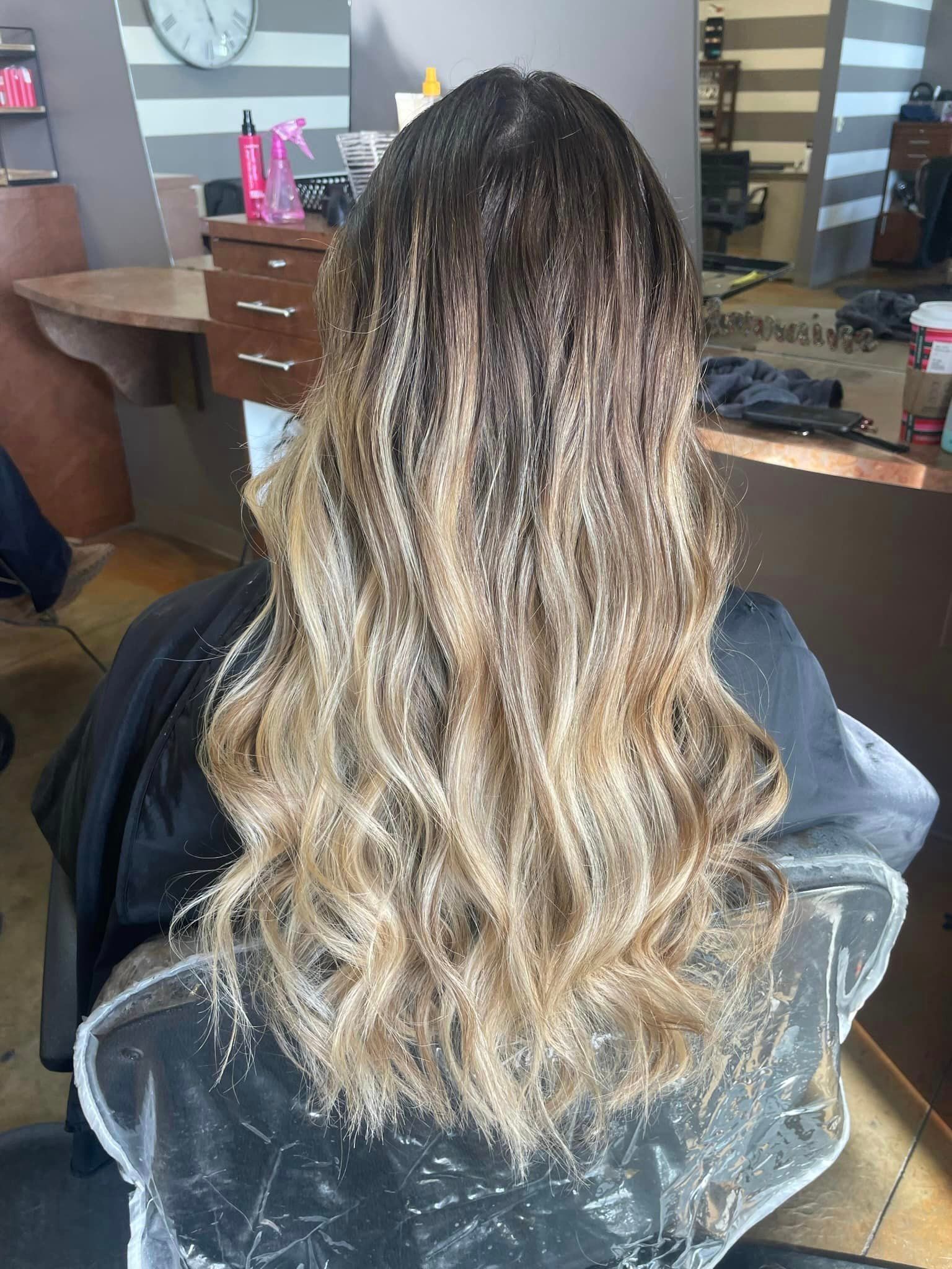 A woman with long blonde hair is sitting in a chair in a salon.