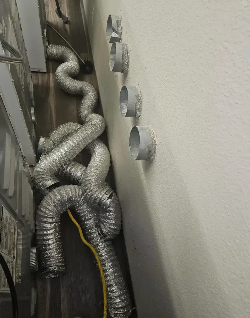Coiled silver ventilation ducts and cables running along a wall in a utility space