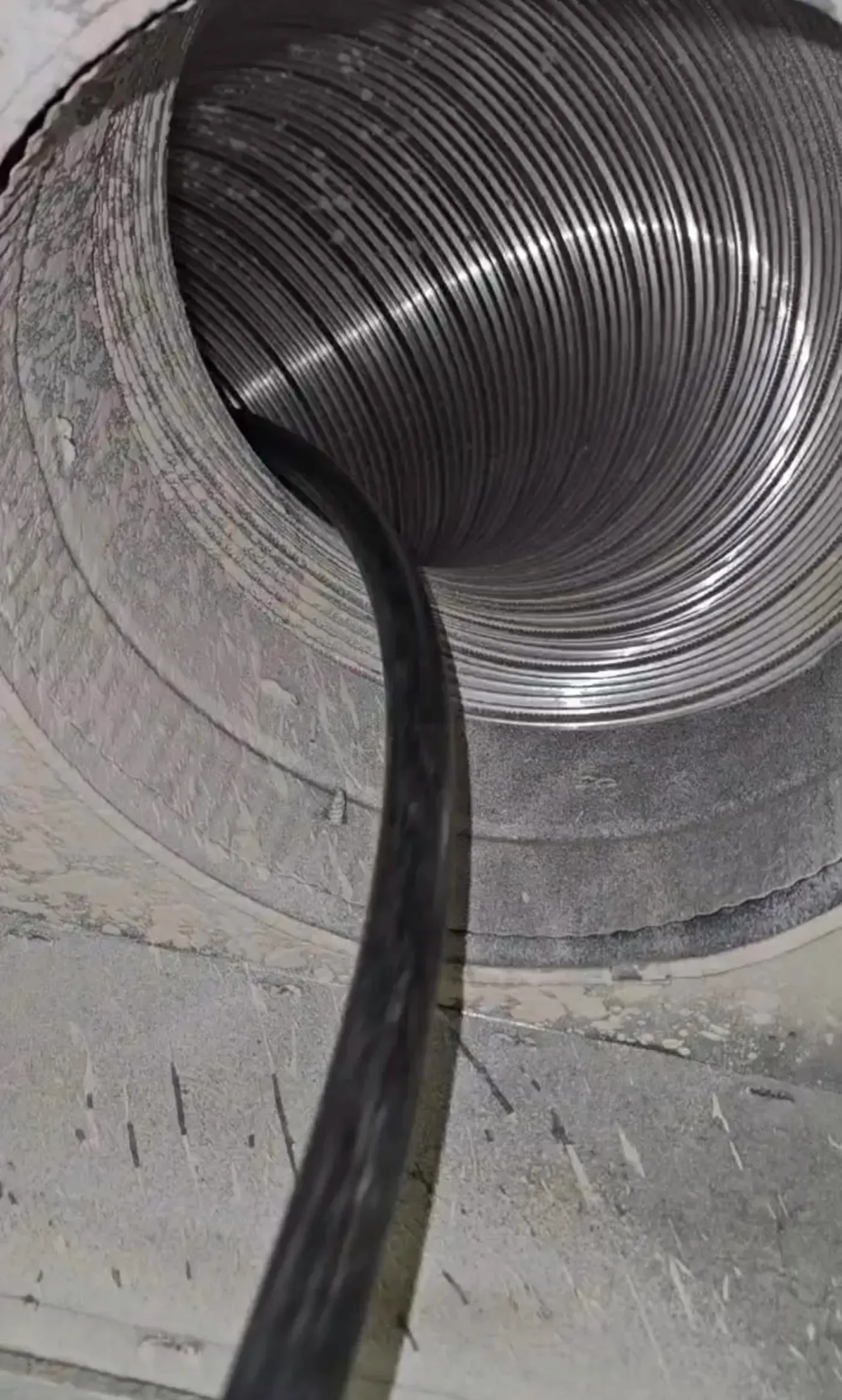 Black cable feeding into a large coiled metal duct or tube inside a concrete opening