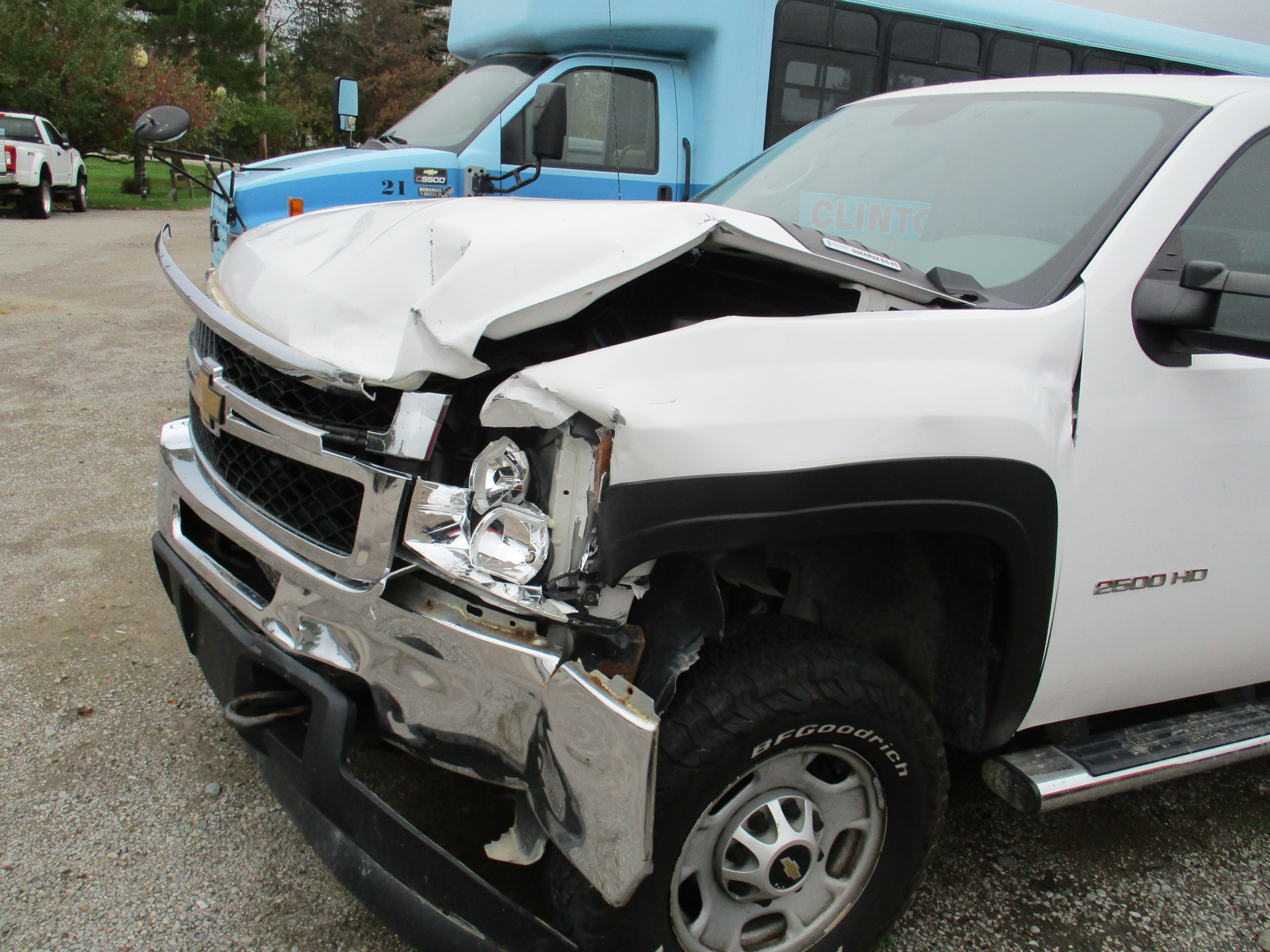 White Chevy pickup truck with front-end damage, parked near a blue bus.