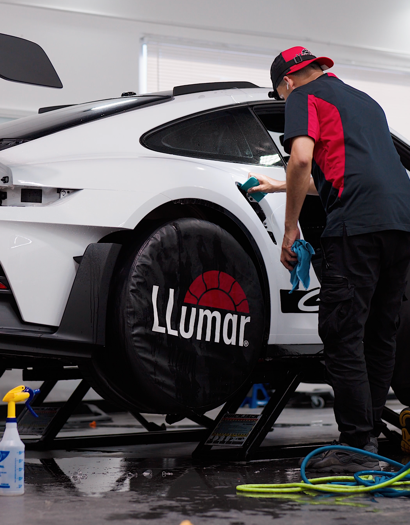 A person cleaning a white sports car's window.  The car is on a lift with wheel covers labeled 