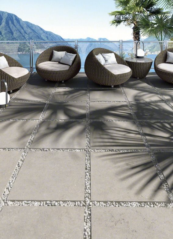 Patio con poltrone in vimini, vista sul lago di montagna e ombre degli alberi sulle piastrelle in pietra