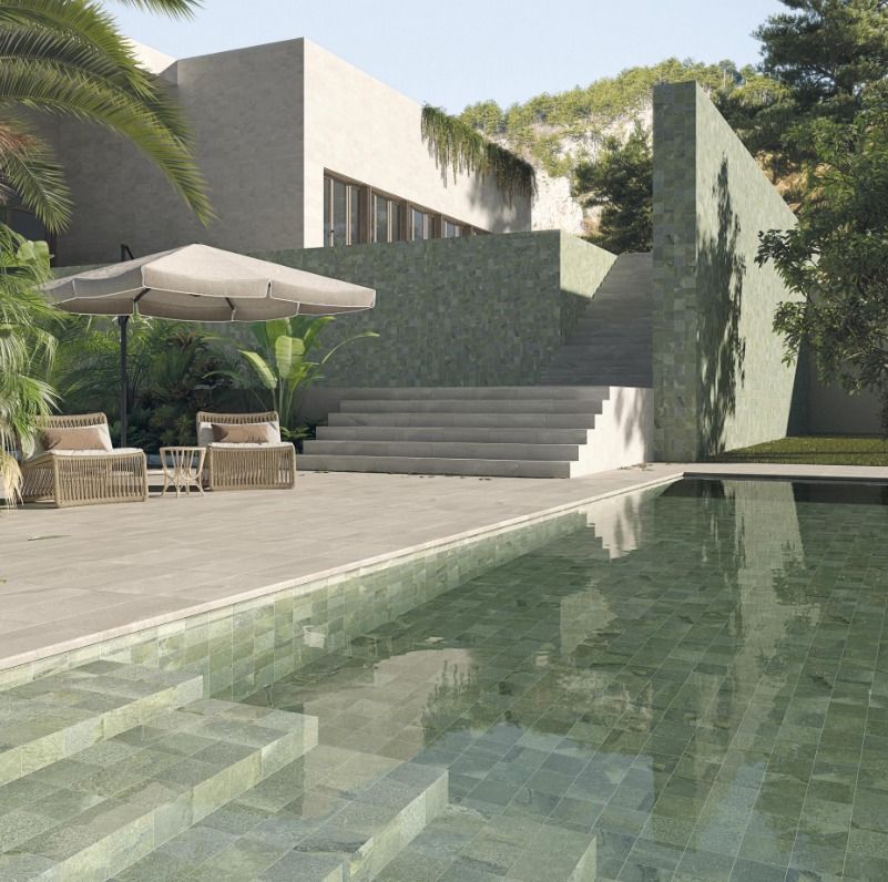 Casa moderna con piscina, sedie da patio e ombrellone accanto a una scalinata bianca e a una vegetazione rigogliosa.
