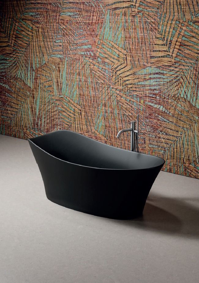 Vasca da bagno nera freestanding con rubinetto cromato davanti a una parete decorata con mosaico