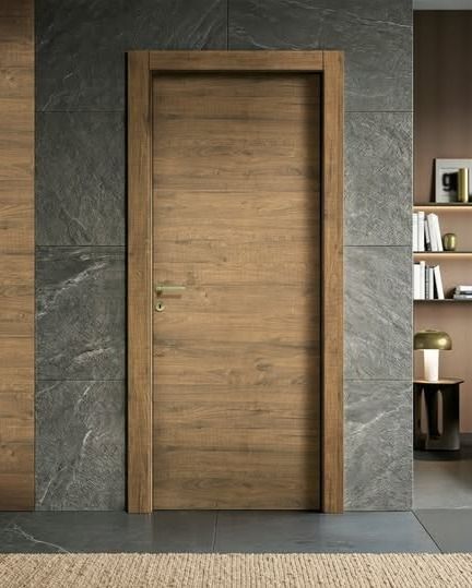 Porta moderna in legno incassata in una parete di pietra scura, con una piccola libreria visibile sulla destra.
