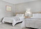 Bright bedroom with two white beds, a lamp, and light striped wallpaper