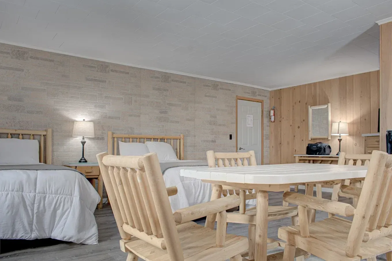 Bright dining room with wooden table and chairs, beige stone walls, and two twin beds in the background