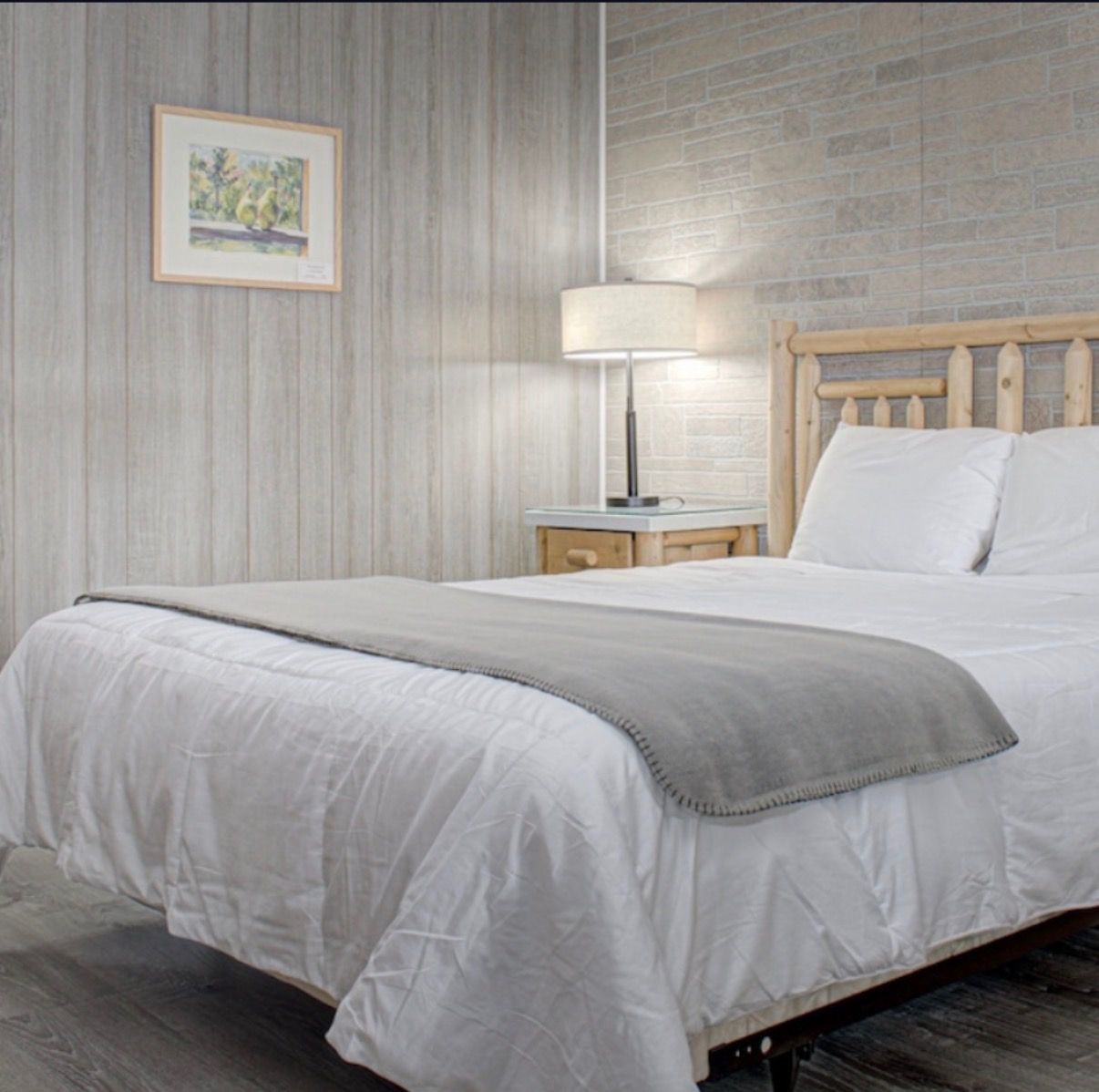 Minimal bedroom with a neatly made bed, gray accents, bedside lamp, and framed wall art.