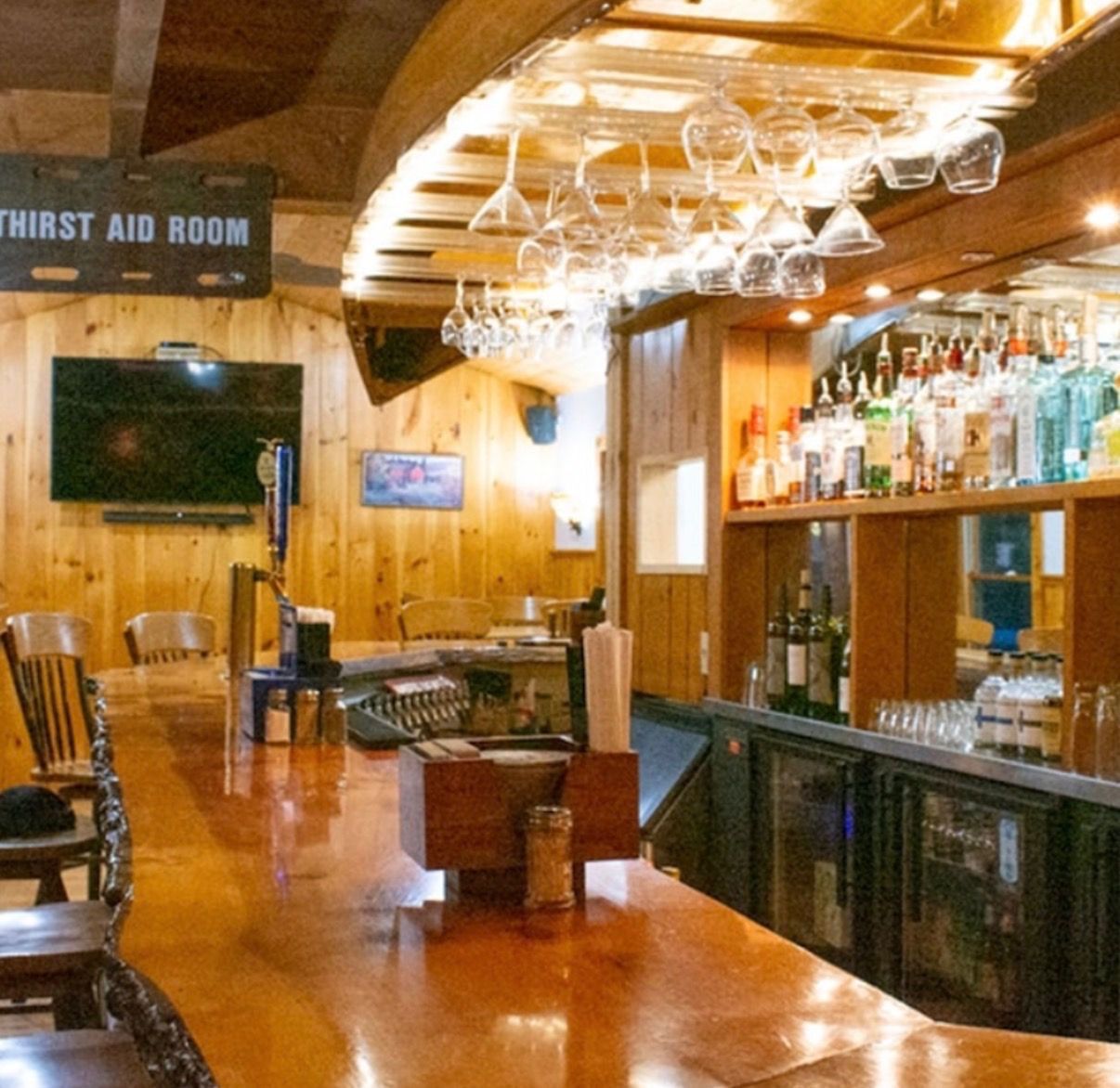Wood-paneled bar with polished wooden counter, hanging glassware, and liquor bottles behind the bar