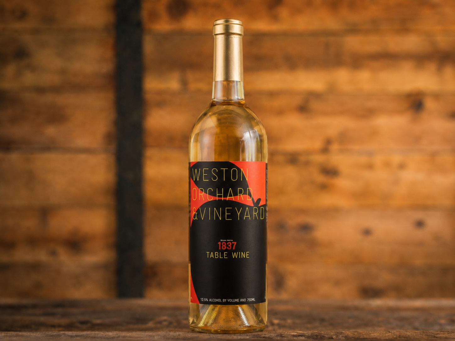 A bottle of peach wine is sitting on a wooden table next to two peaches.