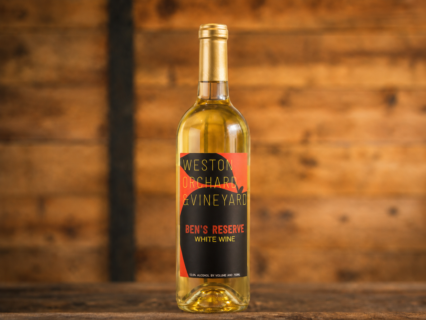 A bottle of peach wine is sitting on a wooden table next to two peaches.