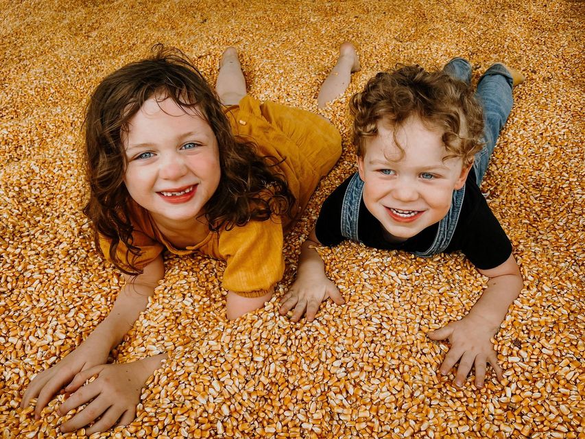 A boy and a girl are laying in a pile of corn.