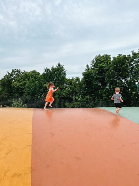Two children are jumping on a bouncy mat in a park.