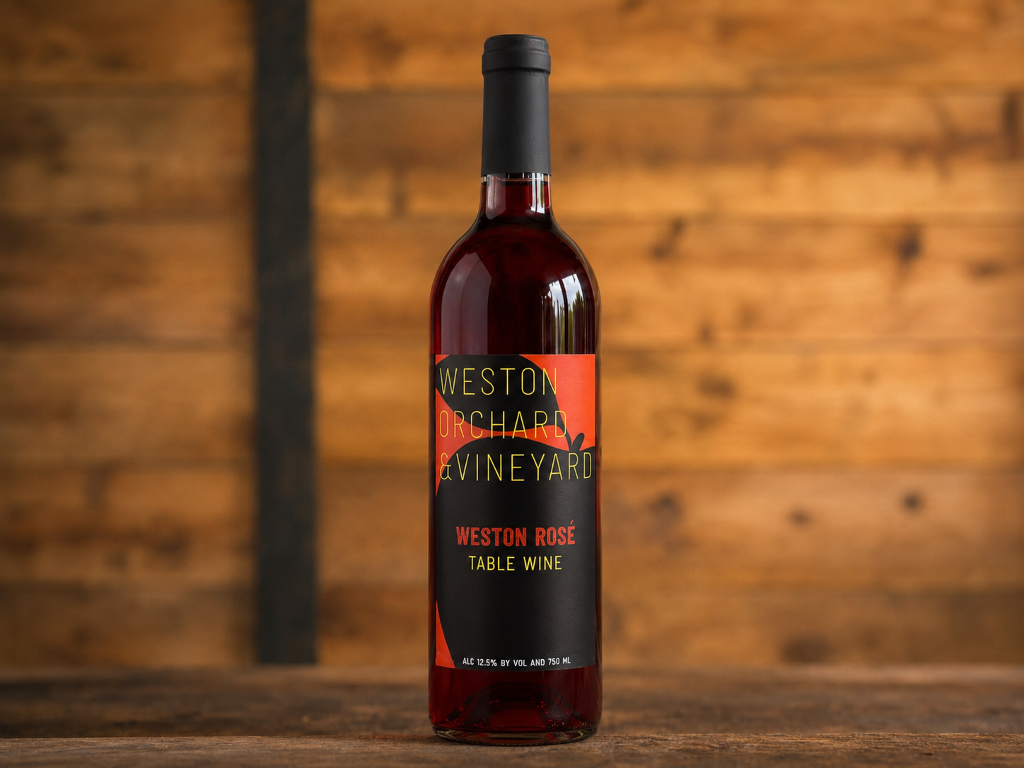 A bottle of peach wine is sitting on a wooden table next to two peaches.