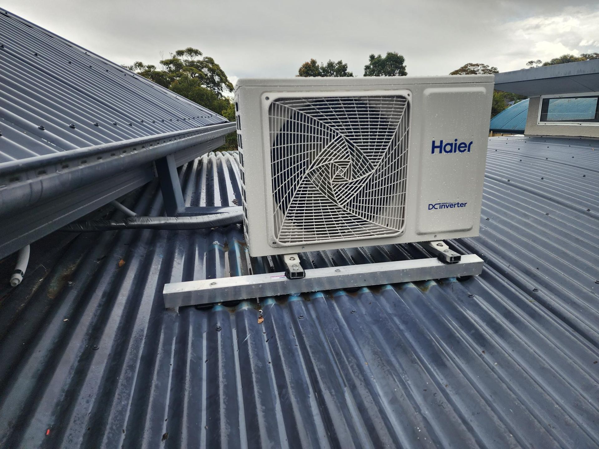 Haier air conditioner unit mounted on a corrugated metal roof. Cloudy sky in background.