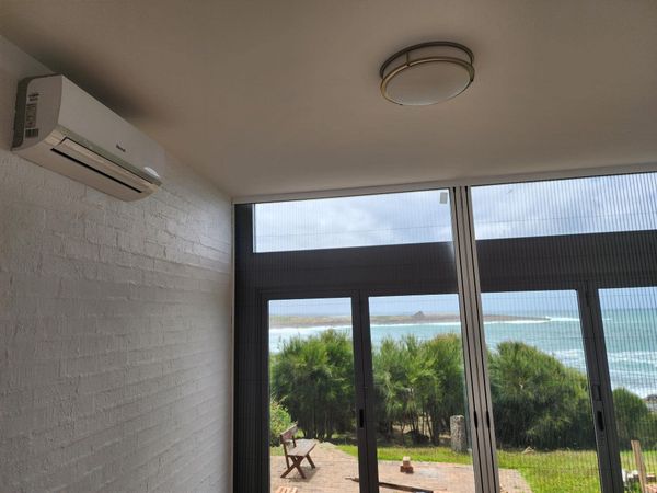 Air conditioner on textured wall, window overlooking ocean and vegetation in Nowra