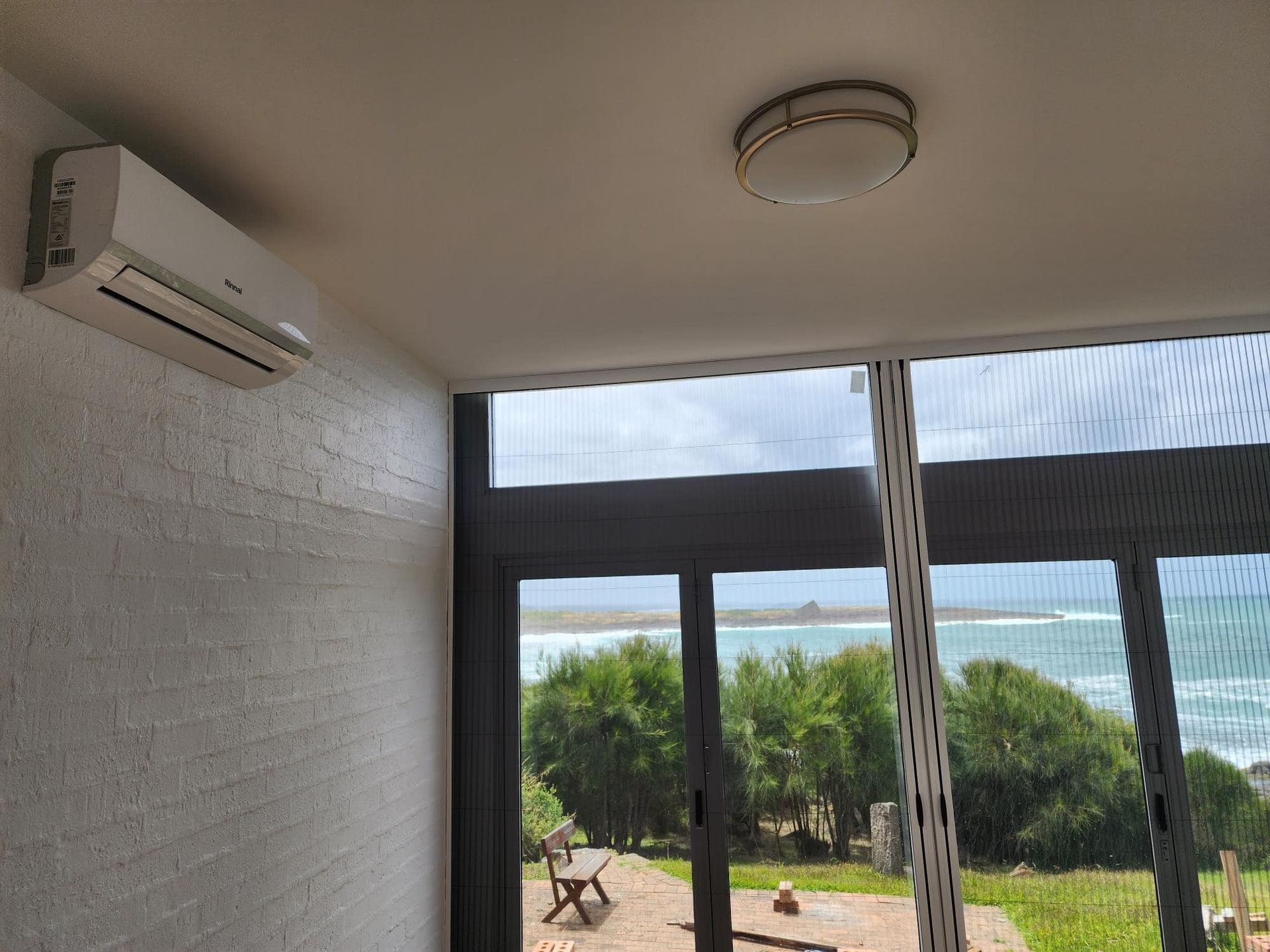 Air conditioner on textured wall, looking out to ocean view through screen door.