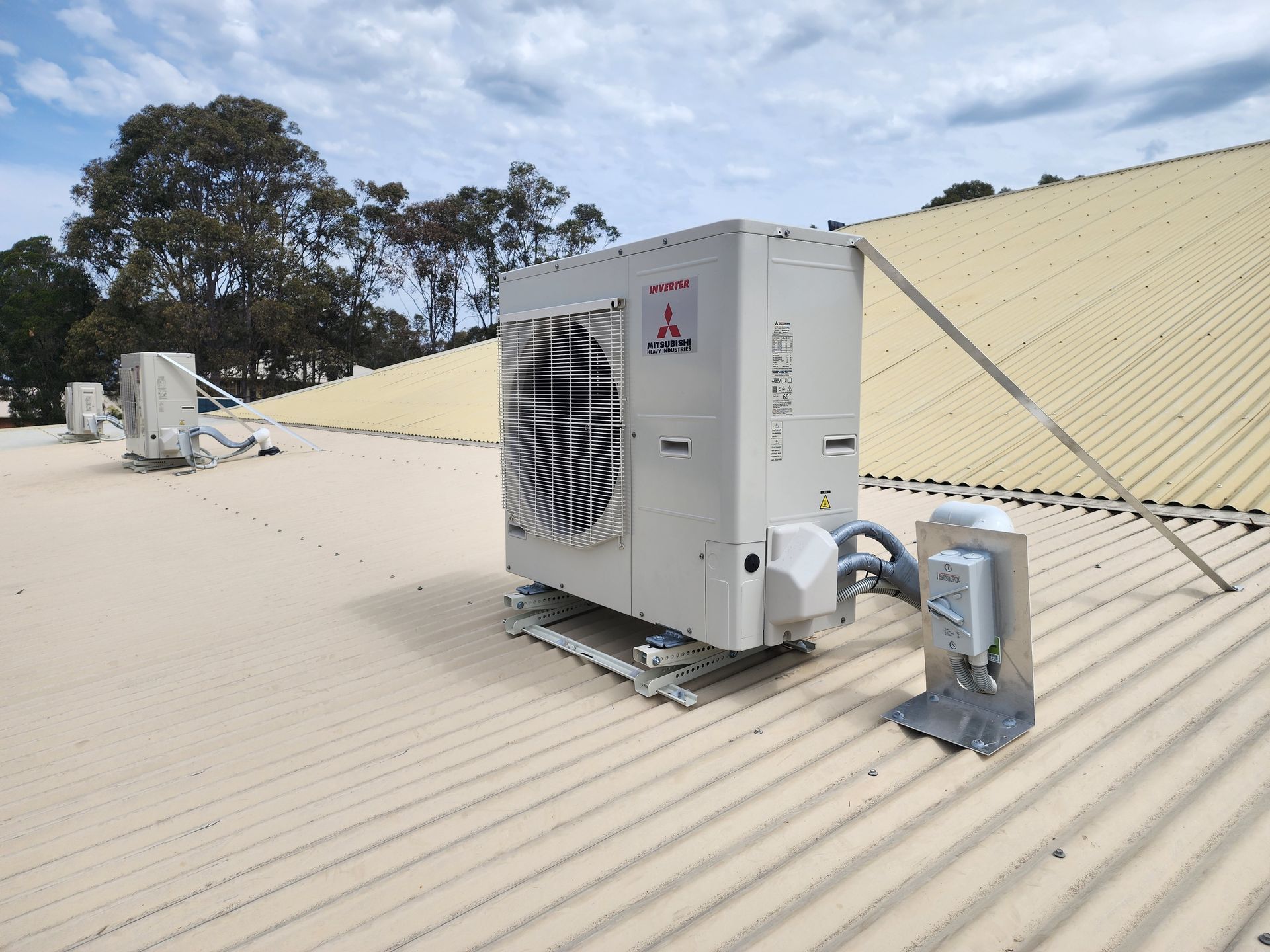 Air conditioning unit on a corrugated roof with support brackets under a cloudy sky in Nowra