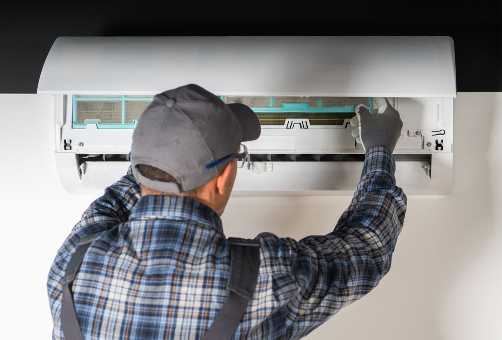 Two Denali Air Conditioning workers in work shirts installing an air conditioner unit next to a building in Nowra