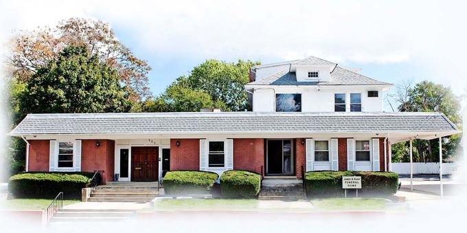 Brick house with white trim, red shutters, and a large porch surrounded by trees and shrubs
