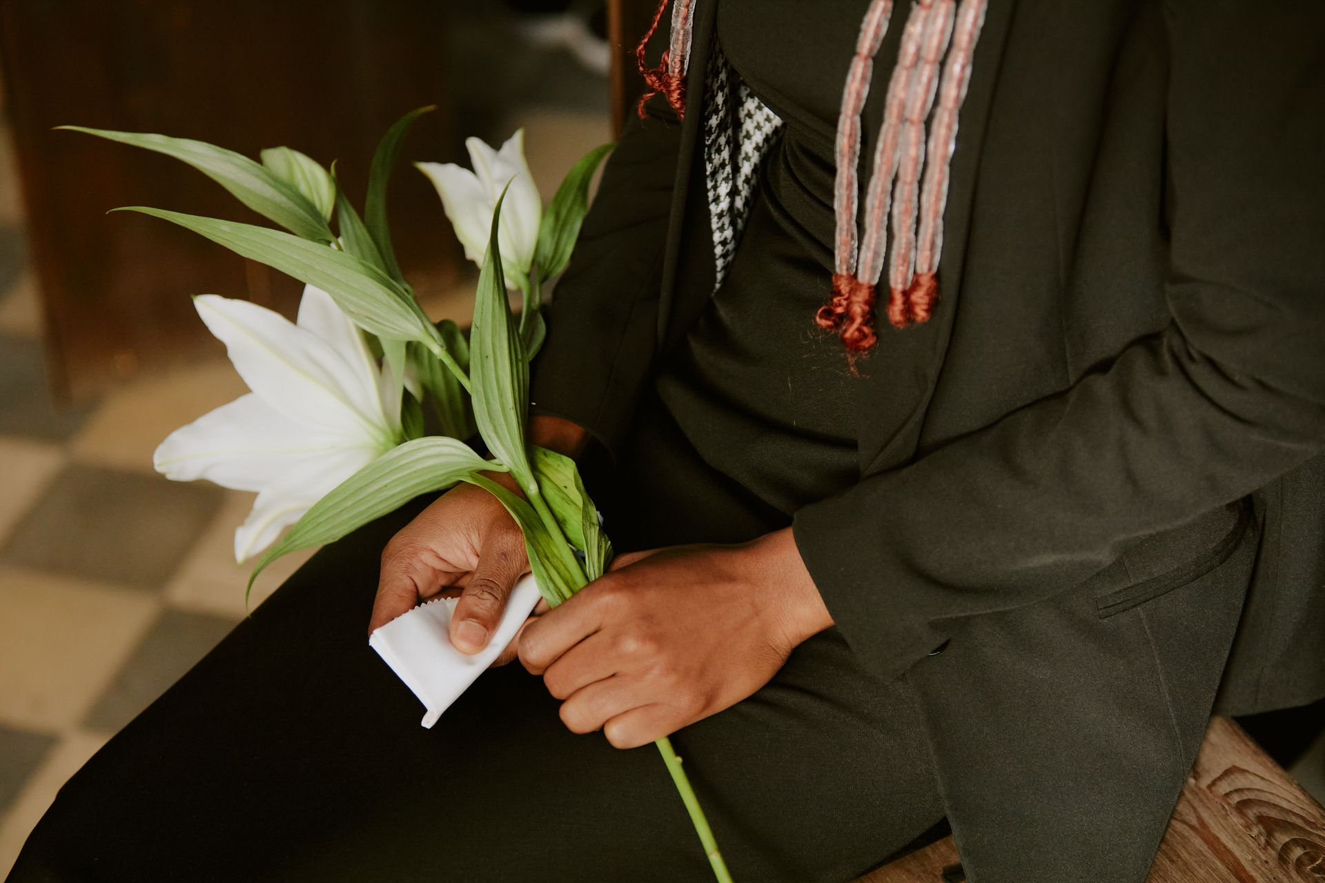 Person holding white lilies and a folded note while seated in a dark outfit