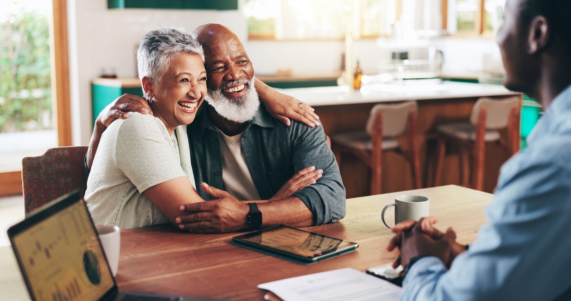 Smiling couple seated at a table in a home, talking with a person across from them holding a pen.