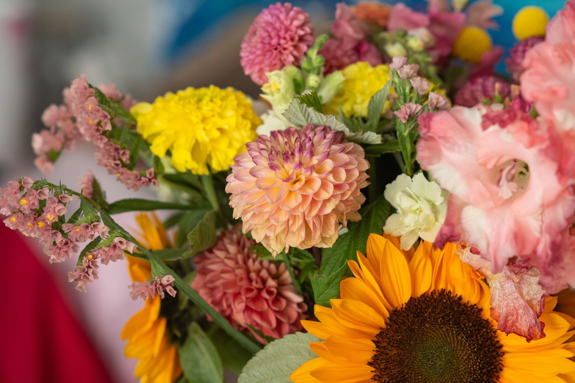 Colorful bouquet of pink, yellow, and orange flowers, including a sunflower, in a soft-focus setting