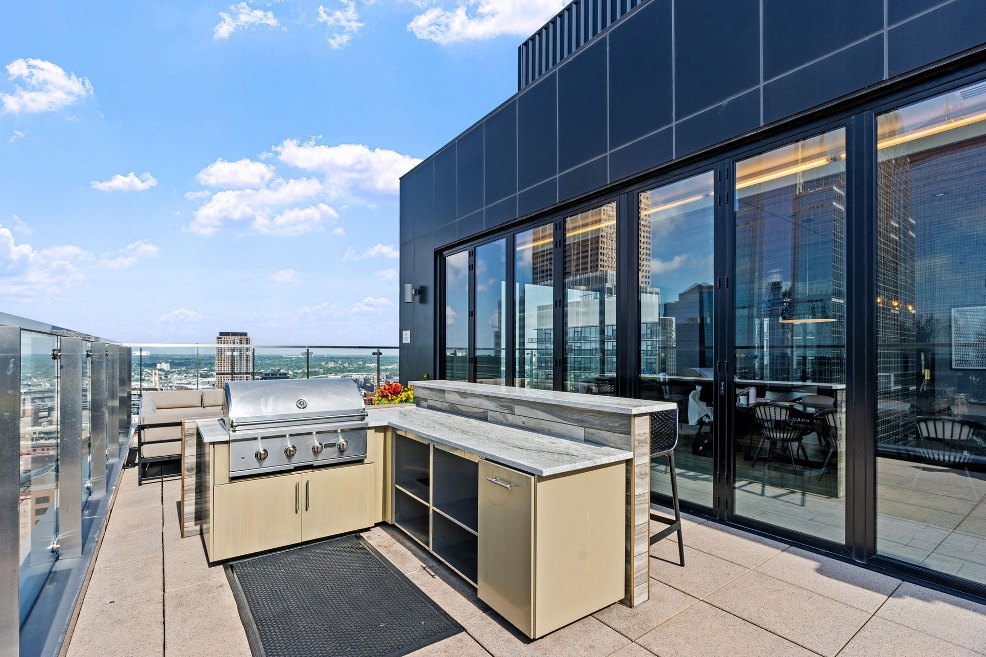Rooftop patio with grill and outdoor kitchen, modern building, city view, sunny day.