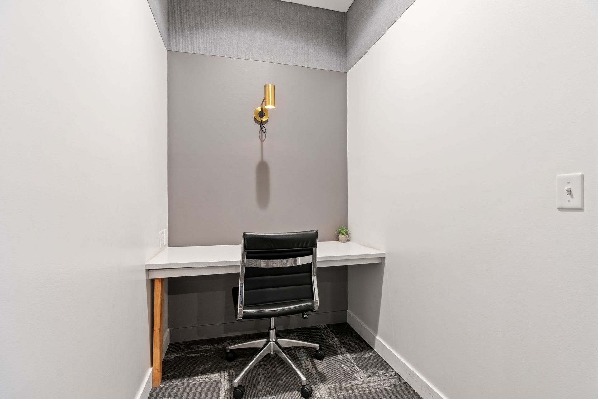 A small office nook with a desk, chair, and a wall-mounted light.