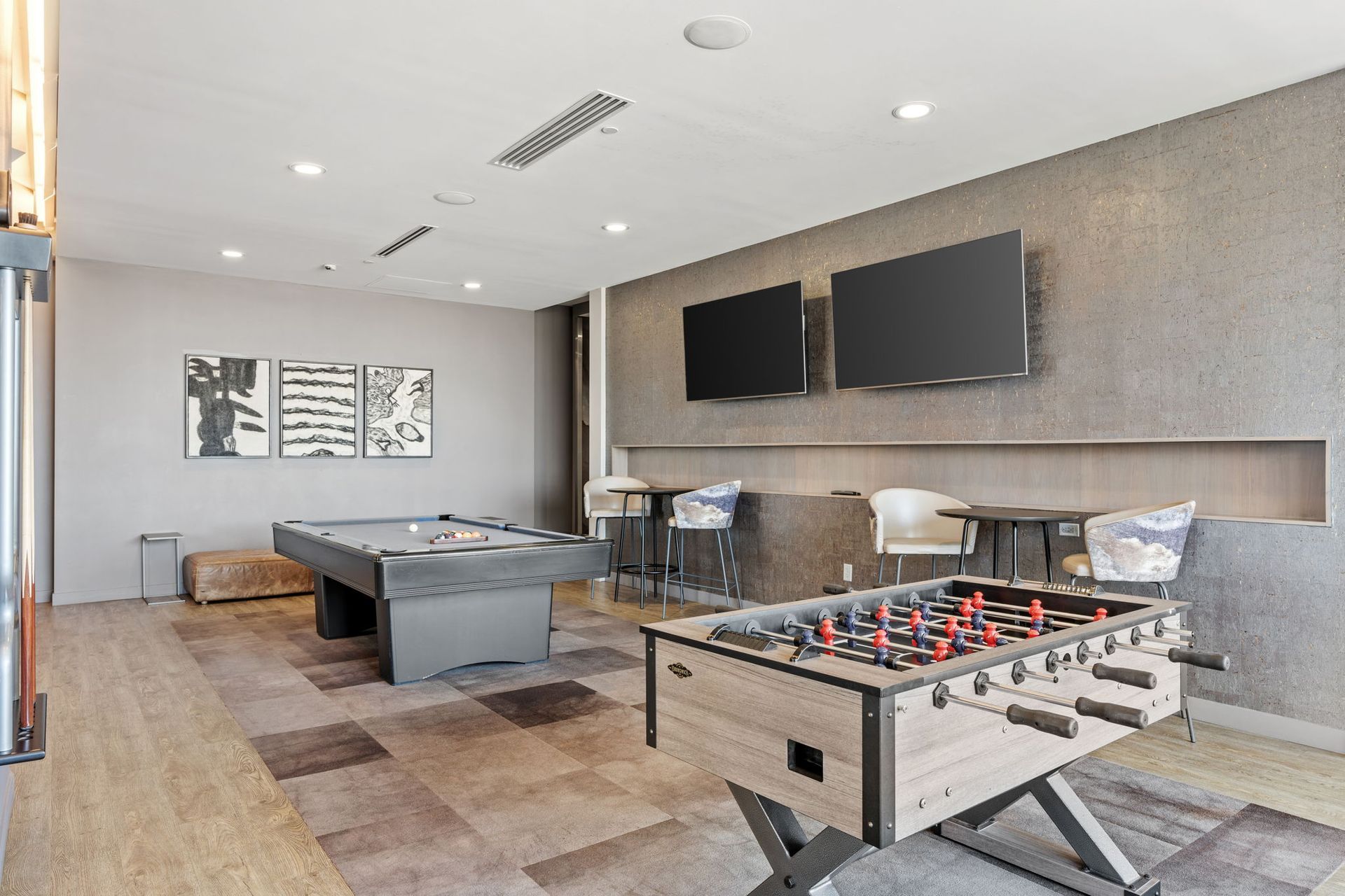 Game room with pool table, foosball, TVs, seating, and abstract art on the wall.