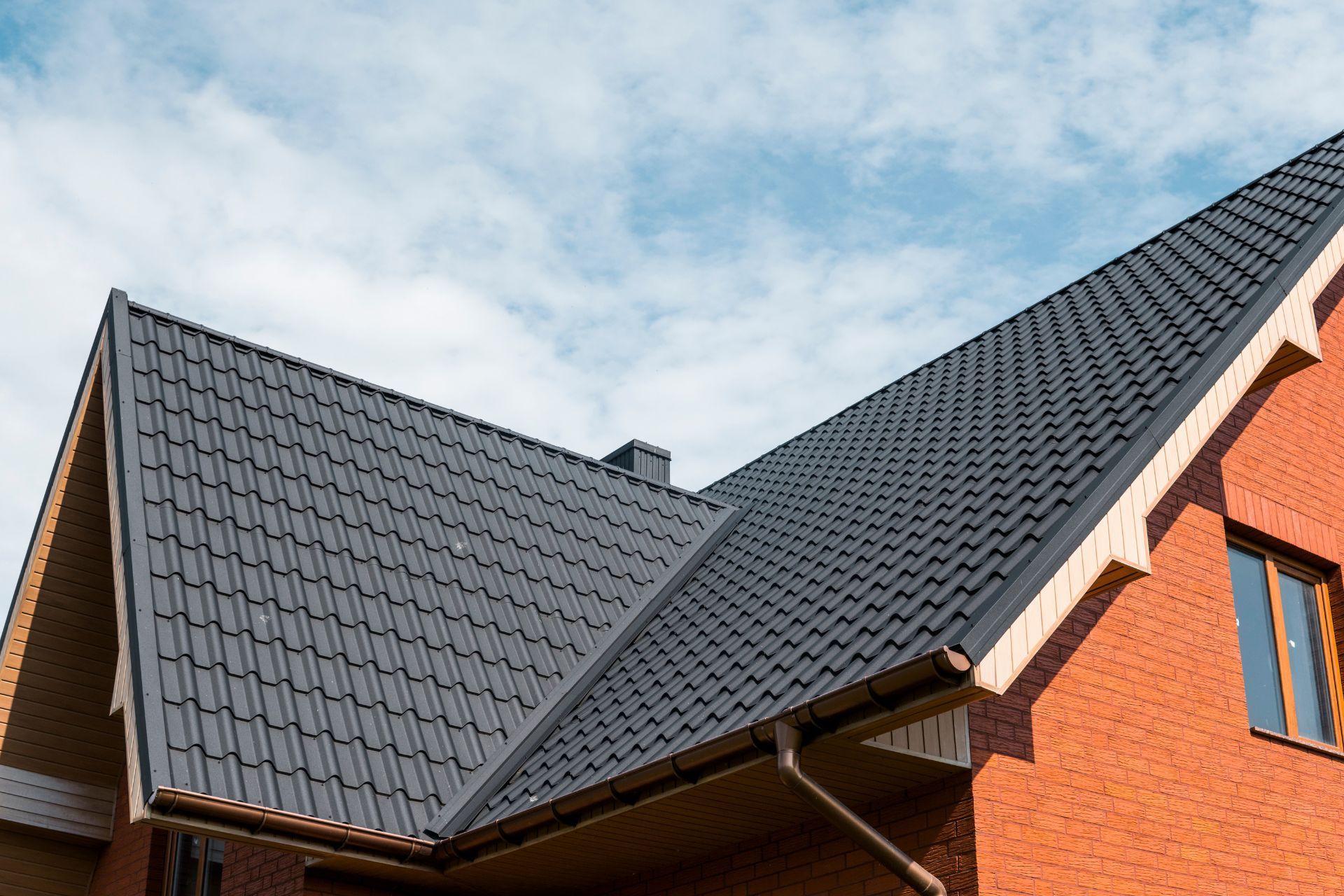 Aerial view of a house roof under repair, with workers and a large white roofing tarp.