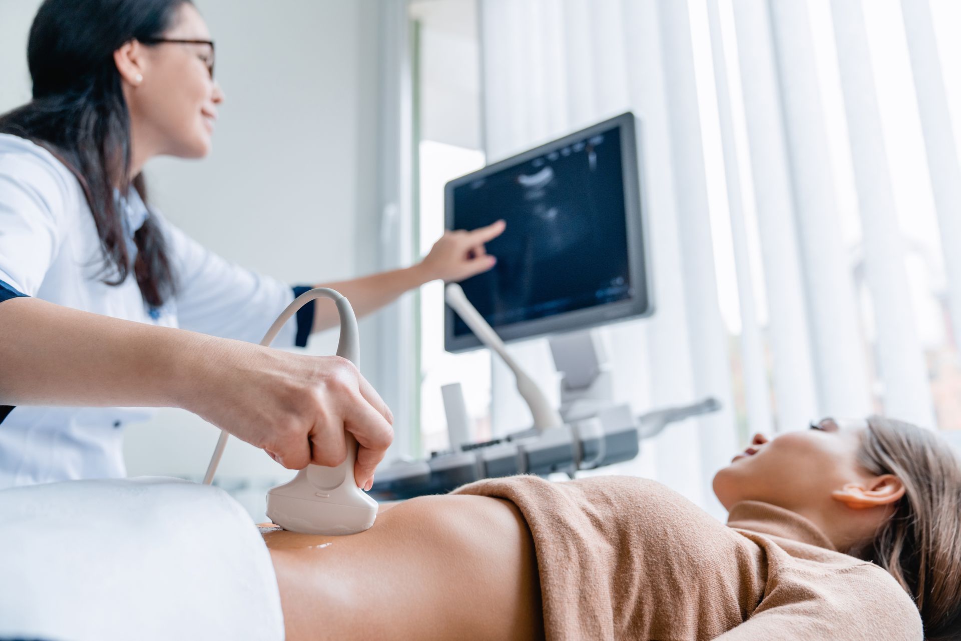 Doctor performing an ultrasound on a patient lying on an exam table while a monitor displays the scan