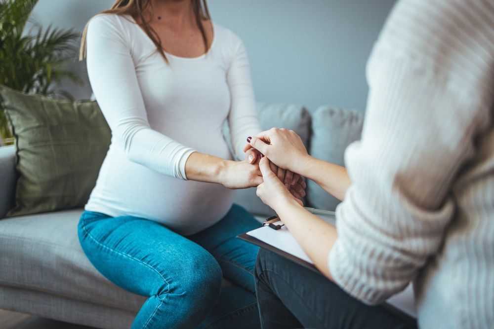 Pregnant person sitting on a couch holding hands with a companion during a calm conversation
