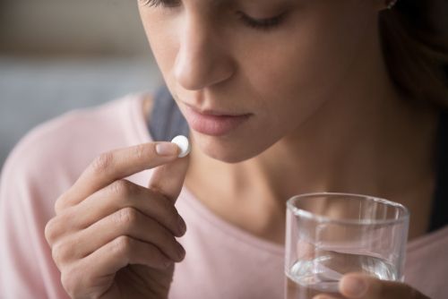 A woman is taking a pill with a glass of water.